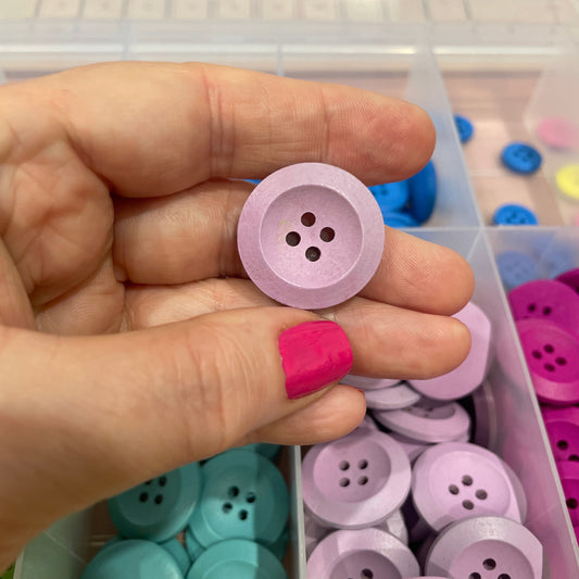 Hand holding a pink button with a container of colorful buttons in the background
