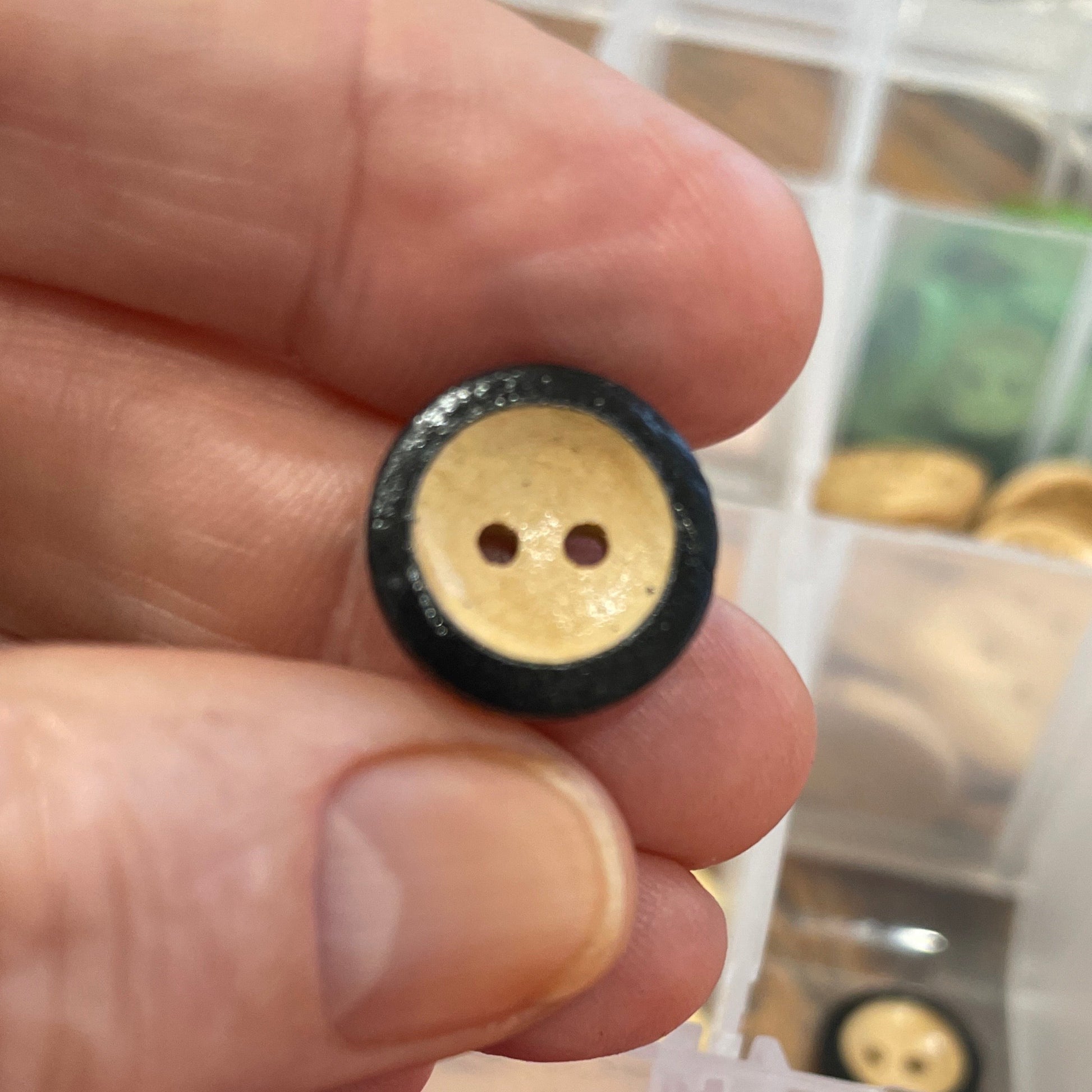 Hand holding a black and gold button with a container of colorful buttons in the background