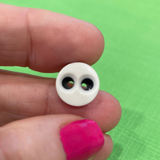 Small white button with black eyes held between fingers against a green background