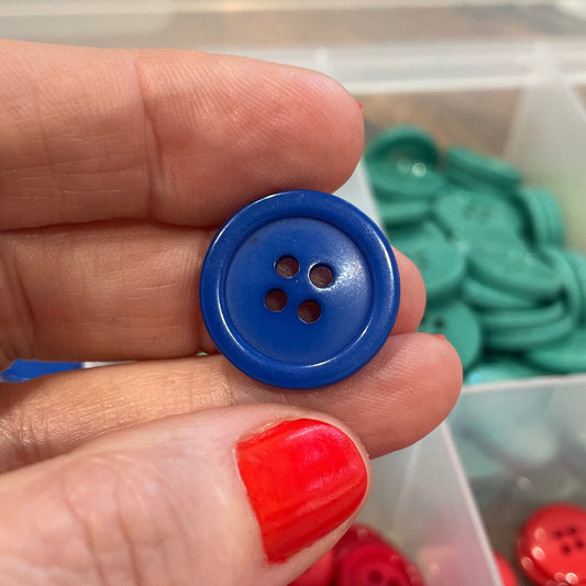 Hand holding a blue button with colorful buttons in a box in the background