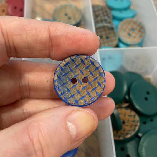 Hand holding a blue textured button with a container of buttons in the background