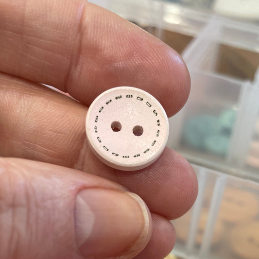 Hand holding a white button with a container of pink buttons in the background