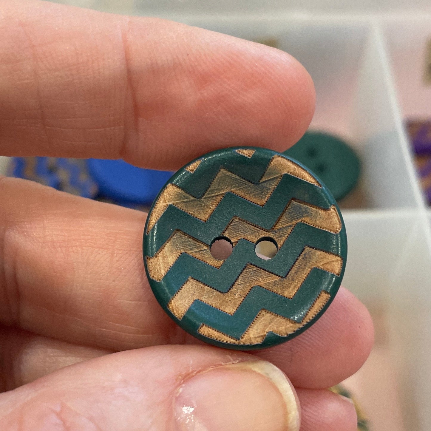 Hand holding a button with a zigzag pattern against a background of various buttons.