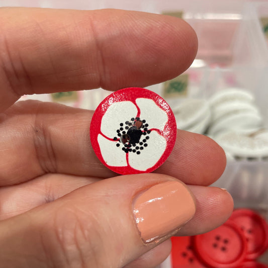 Hand holding a red and white button with a black center against a background of various buttons.