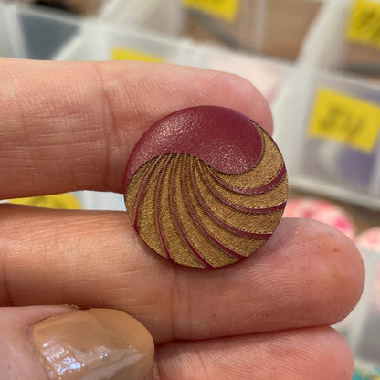 Hand holding a wooden spiral button with a container of buttons in the background