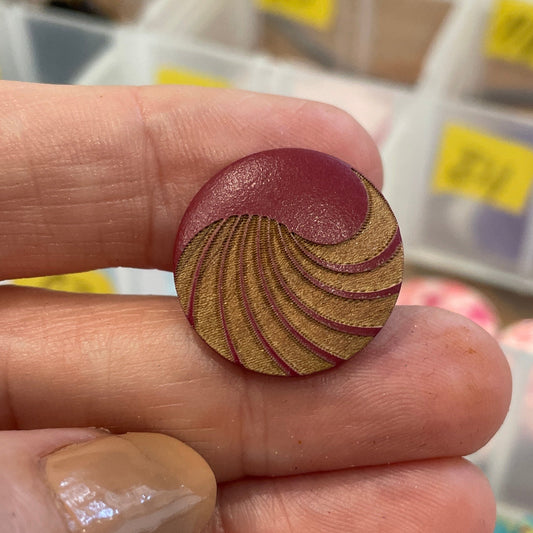 Hand holding a wooden spiral button with a container of buttons in the background