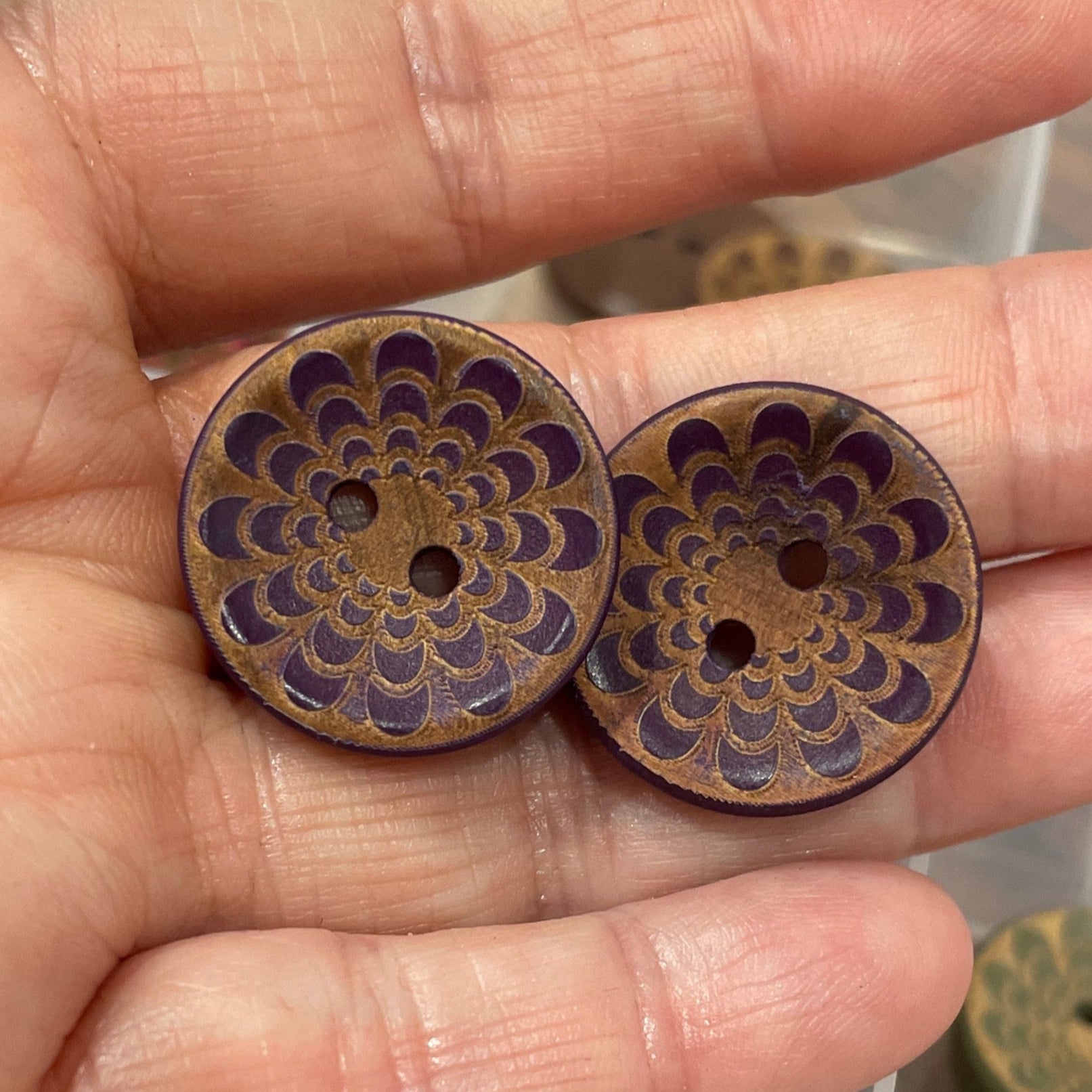 Hand holding decorative buttons with a container of similar buttons in the background