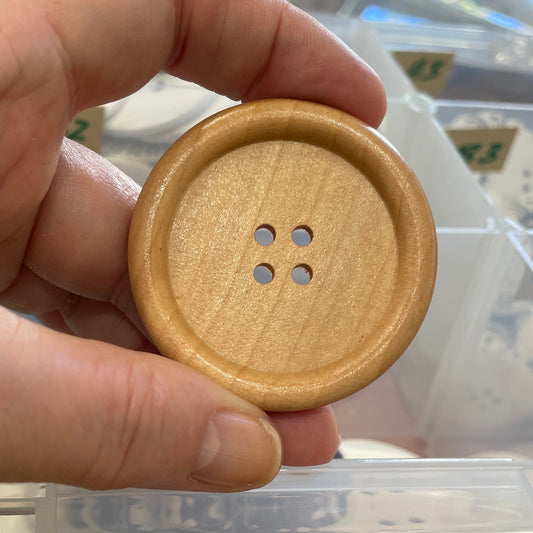 Hand holding a wooden button with a clear plastic container in the background
