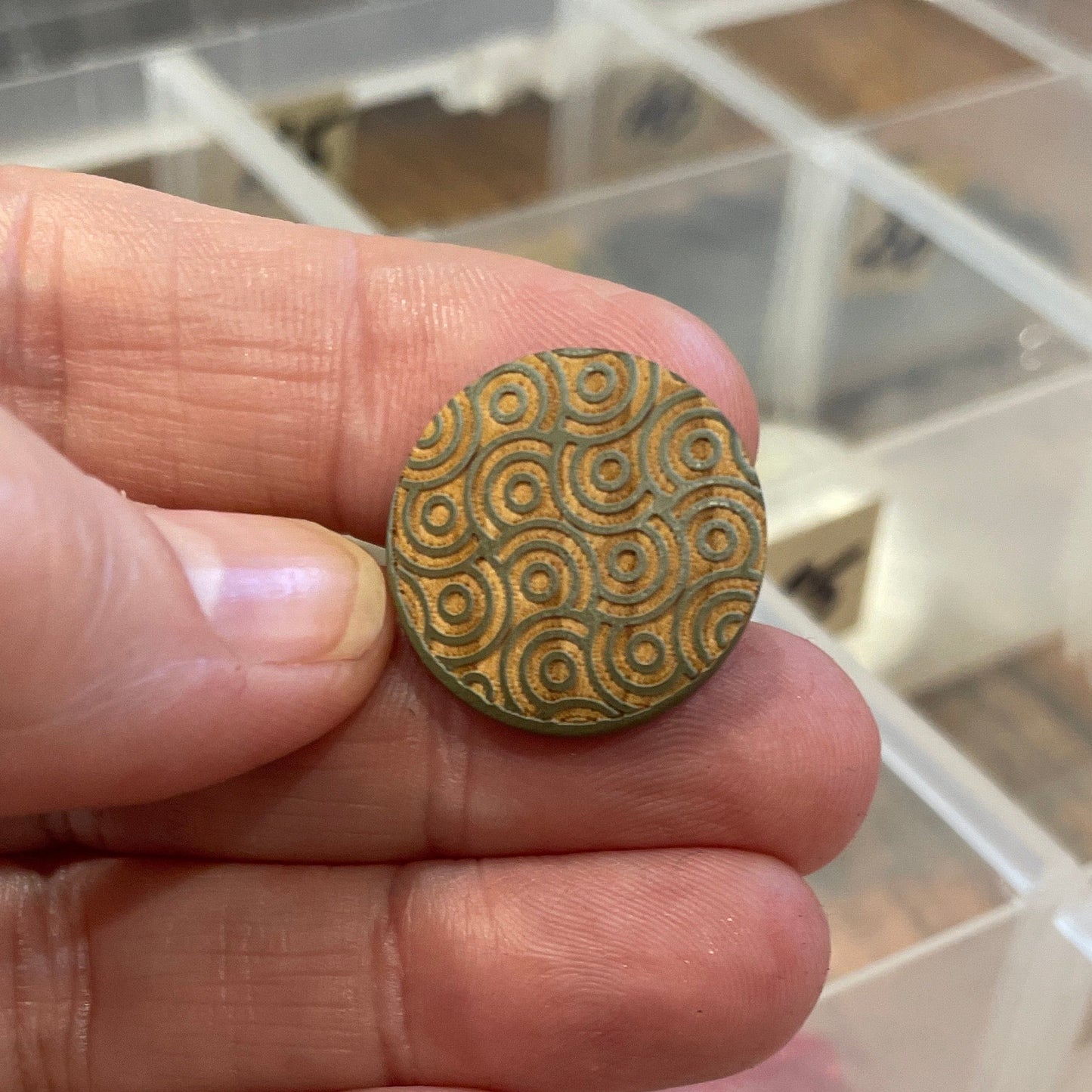 button held between fingers with a blurred background of containers.