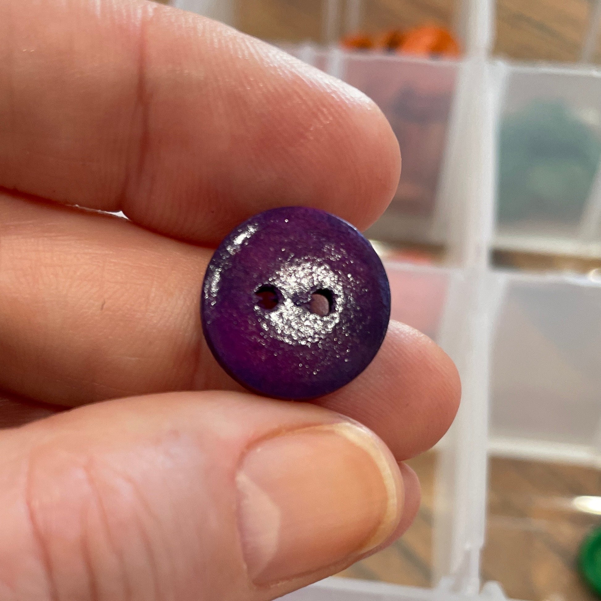 Hand holding a purple button with a container of buttons in the background