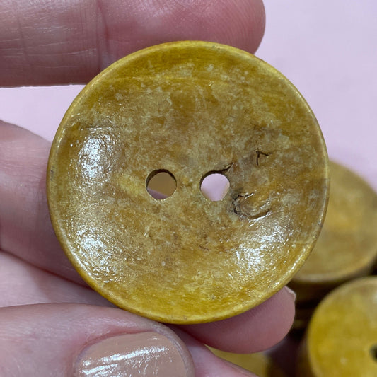 Hand holding a yellow button with more buttons in the background on a pink surface