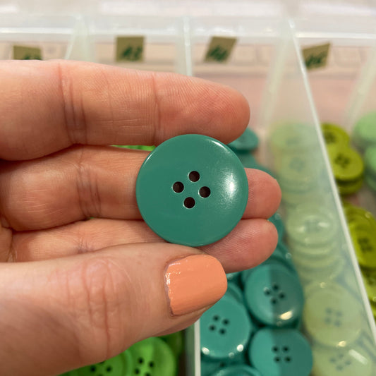 Hand holding a green button with a container of buttons in the background