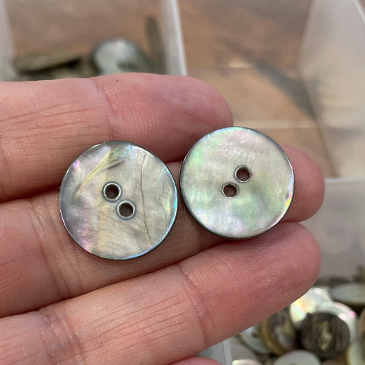 Two buttons held between fingers with a container of buttons in the background