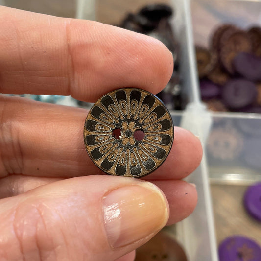 Hand holding a decorative button with a blurred background of button collection