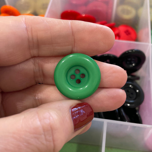 Hand holding a green button with a container of colorful buttons in the background