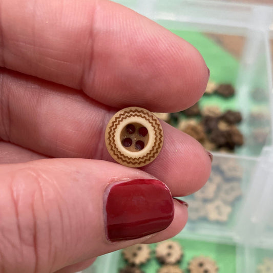 Hand holding a small wooden button with a container of similar buttons in the background