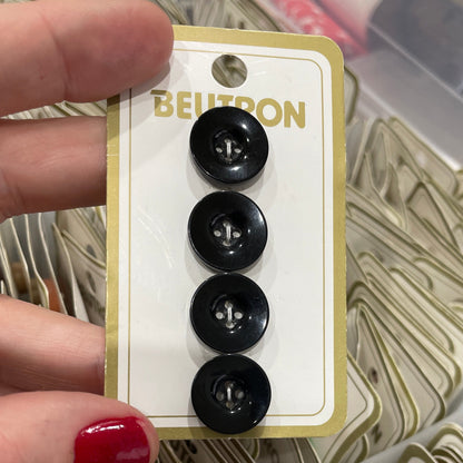 Set of black buttons on a Belton branded card held by a person with red nail polish.