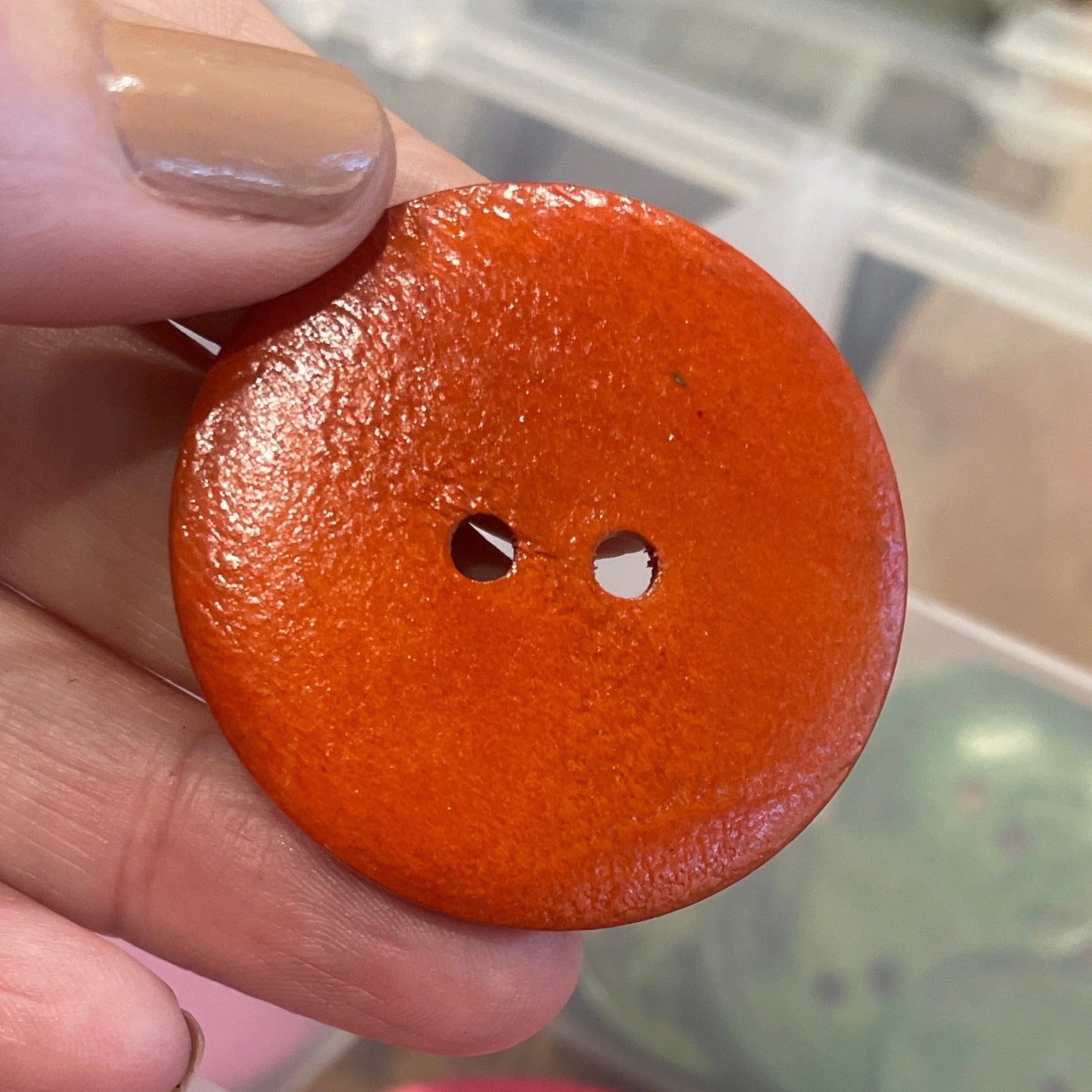 Hand holding a brown button with a container of pink buttons in the background