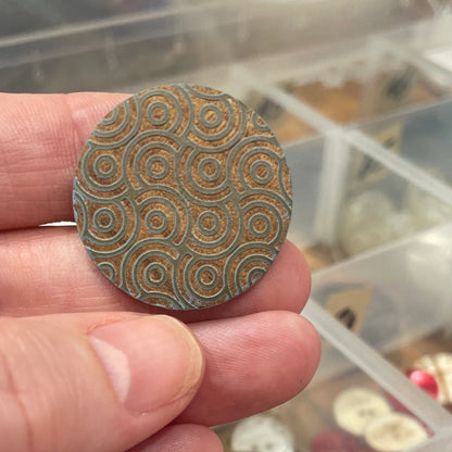 Hand holding a patterned button with a container of buttons in the background
