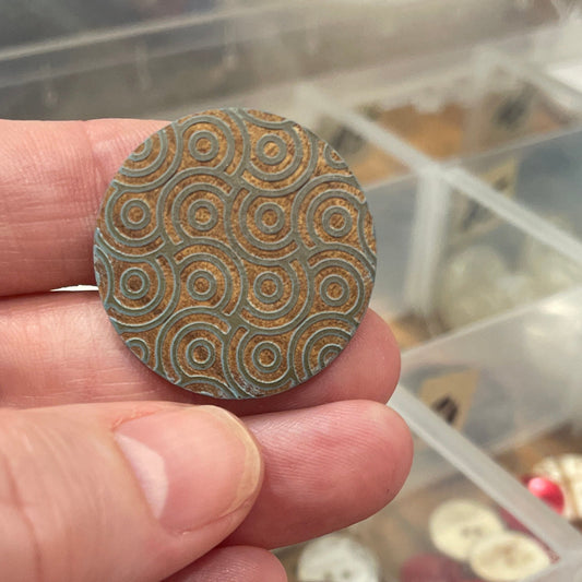 Hand holding a patterned button with a container of buttons in the background