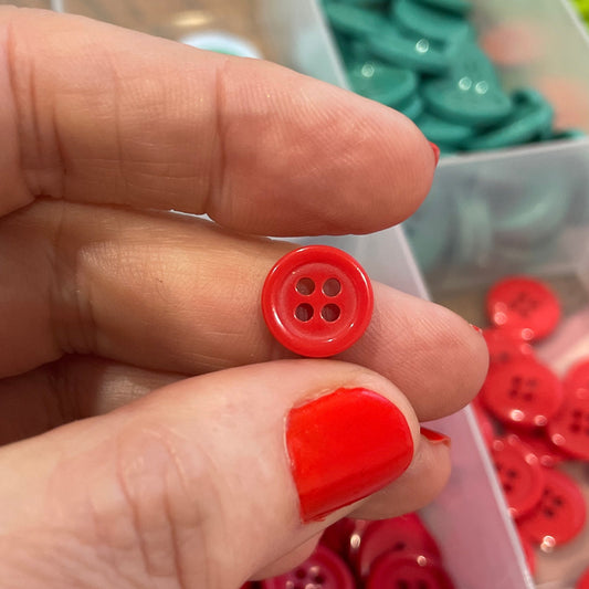 Hand holding a red button with a container of buttons in the background