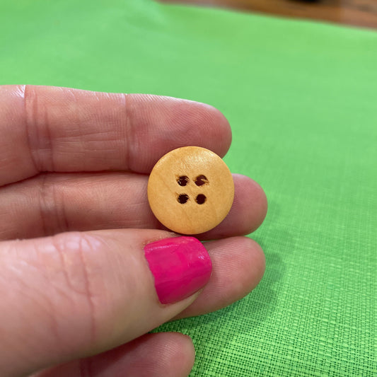 Hand holding a yellow button with four holes against a green background