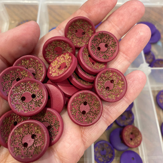 Hand holding a collection of purple buttons with floral patterns, blurred background