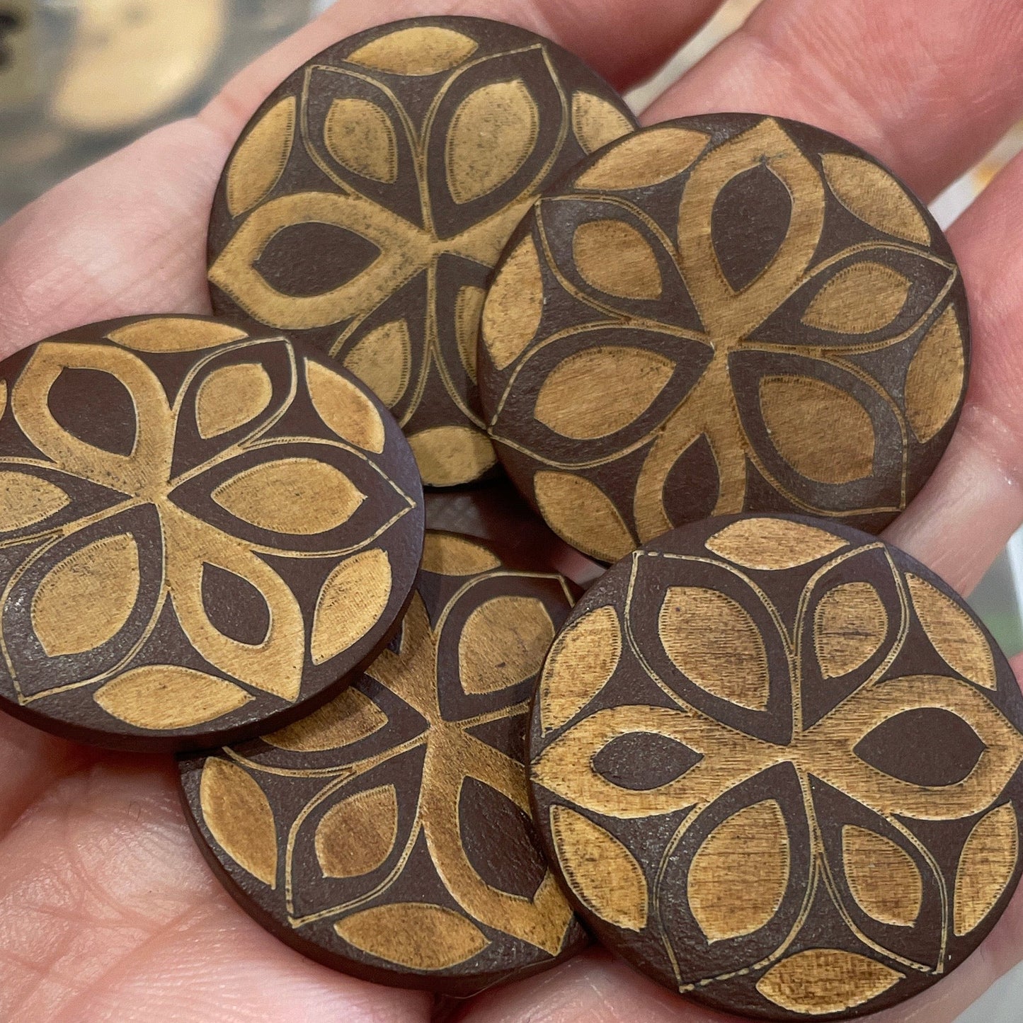 Hand holding wooden buttons with intricate designs in a blurred background of button collection.