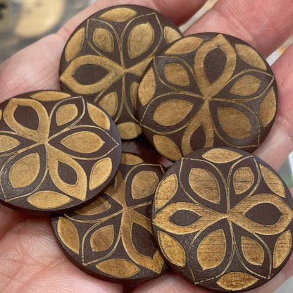Hand holding wooden buttons with intricate designs in a blurred background of button collection.