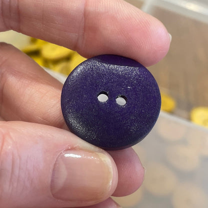 Hand holding a purple button with a clear container of buttons in the background