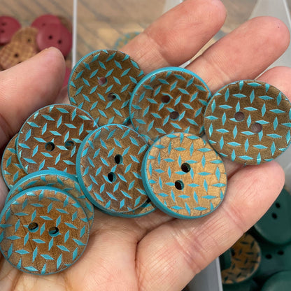 Hand holding five decorative buttons with a textured pattern, in front of a container with more buttons.