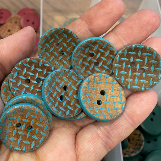 Hand holding five decorative buttons with a textured pattern, in front of a container with more buttons.