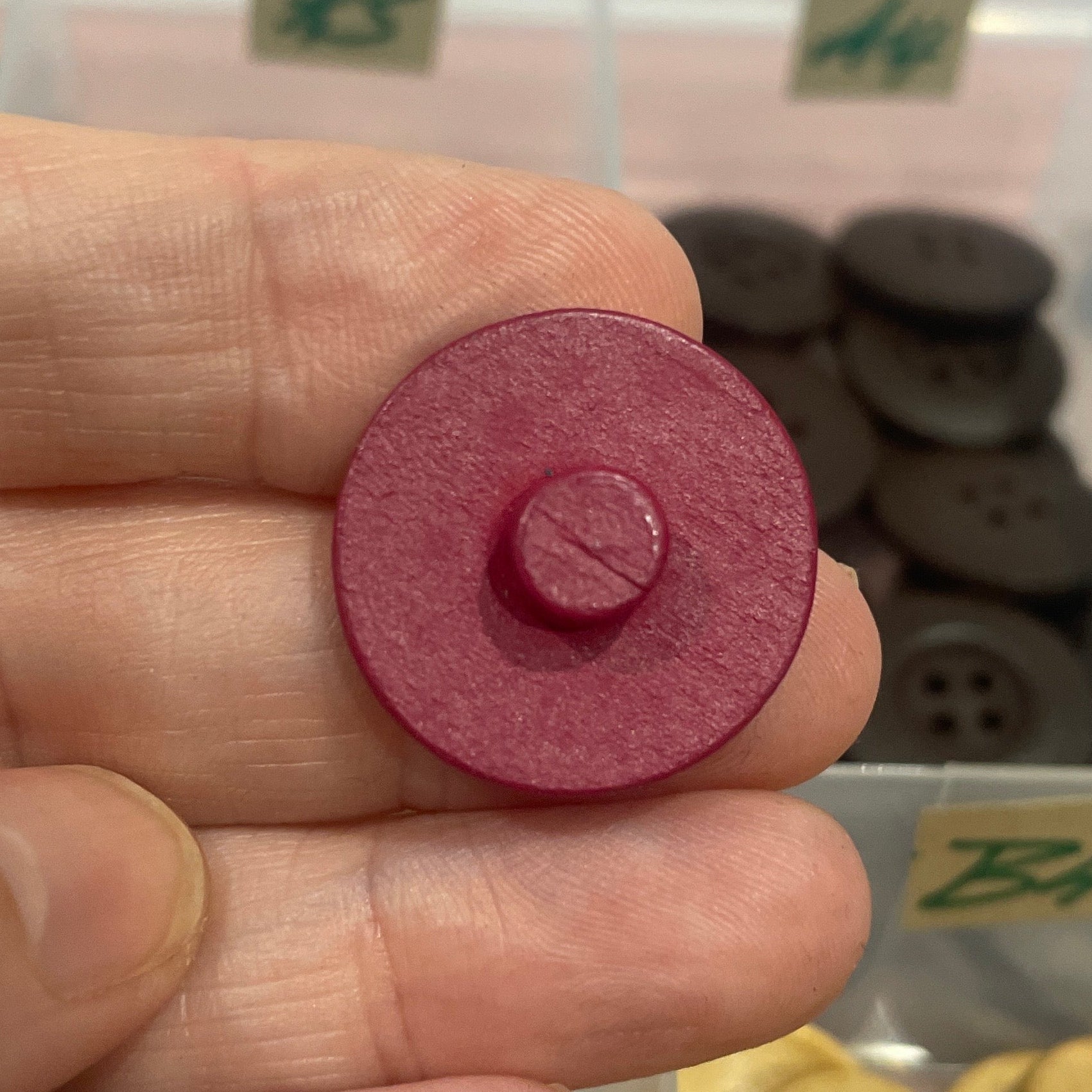 Hand holding a red button with a container of gold buttons in the background