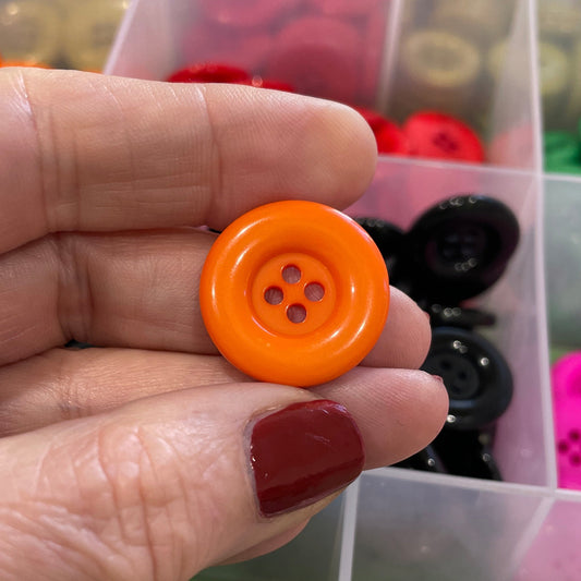 Hand holding an orange button with a background of colorful buttons in a box