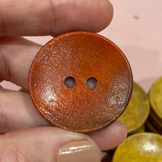 Hand holding a brown button with other buttons on a pink surface