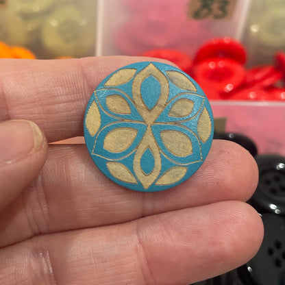 Hand holding a blue button with a colorful button collection in the background.