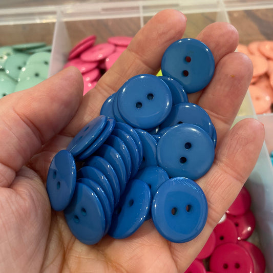 Hand holding blue buttons with a background of colorful buttons in containers.