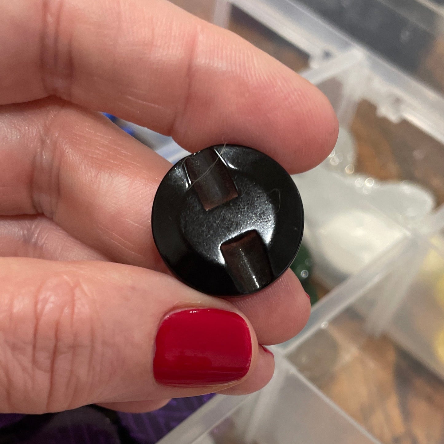 Person holding a black button with a container of various buttons in the background