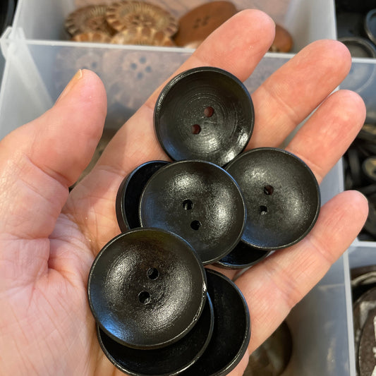 Hand holding black buttons with a container of buttons in the background