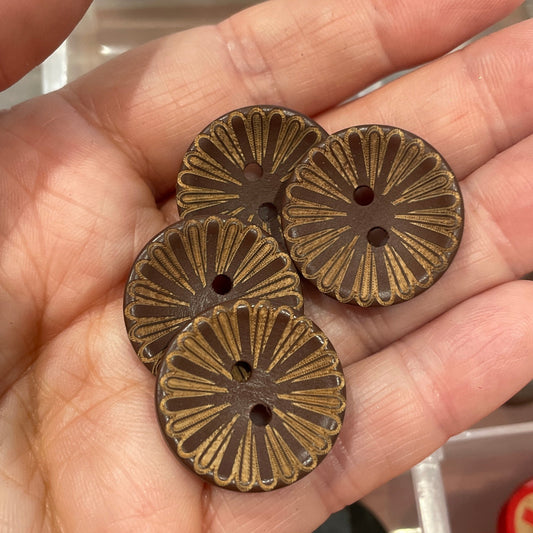 Three bronze buttons held in a hand with a container of buttons in the background.