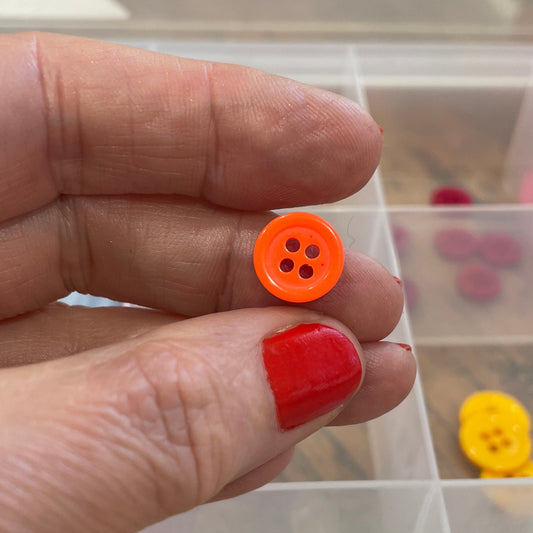 Hand holding an orange button with a clear container of buttons in the background