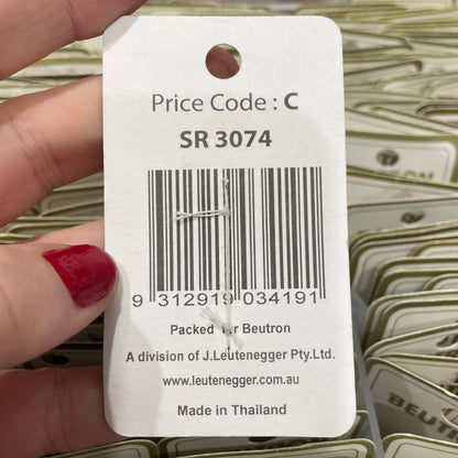 Hand holding a product tag with a barcode and text, with shelves of similar products in the background.