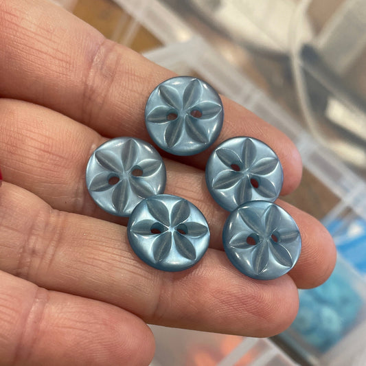 Metal flower-shaped objects held in a hand with a blurred background of a storage box.