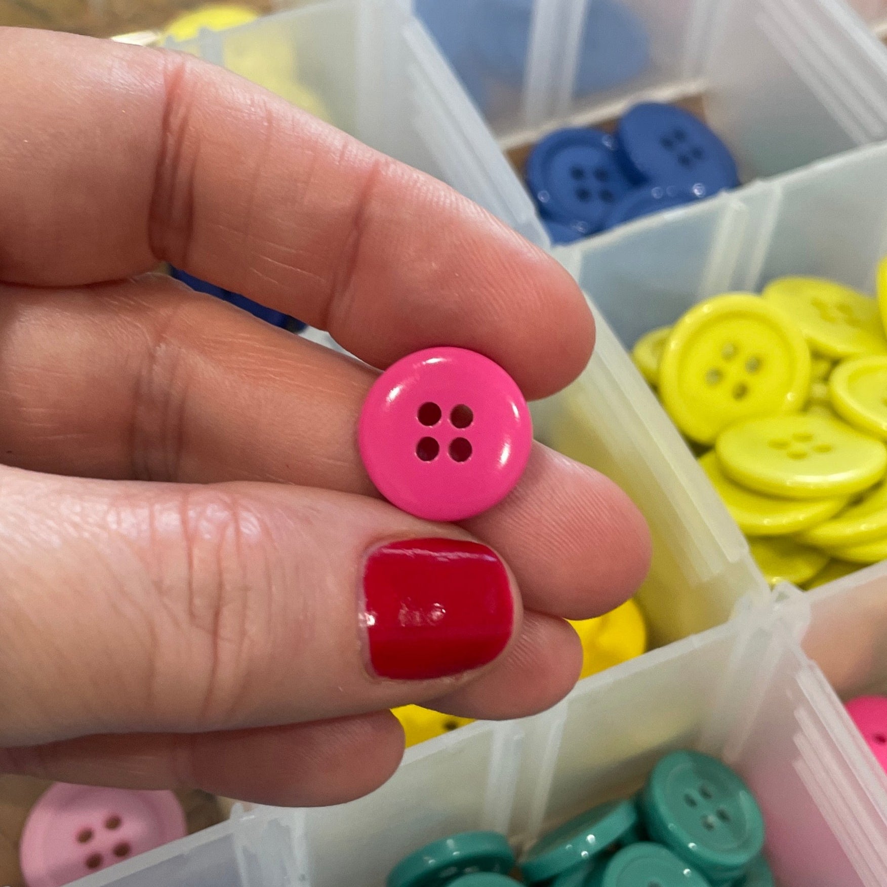 Hand holding a pink button with a container of colorful buttons in the background