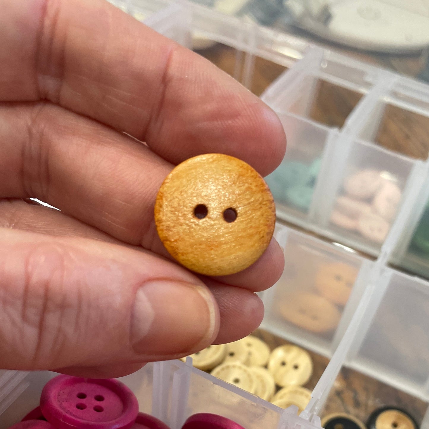 Hand holding a yellow button with a container of buttons in the background