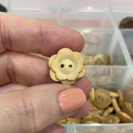 Hand holding a gold button with a container of buttons in the background
