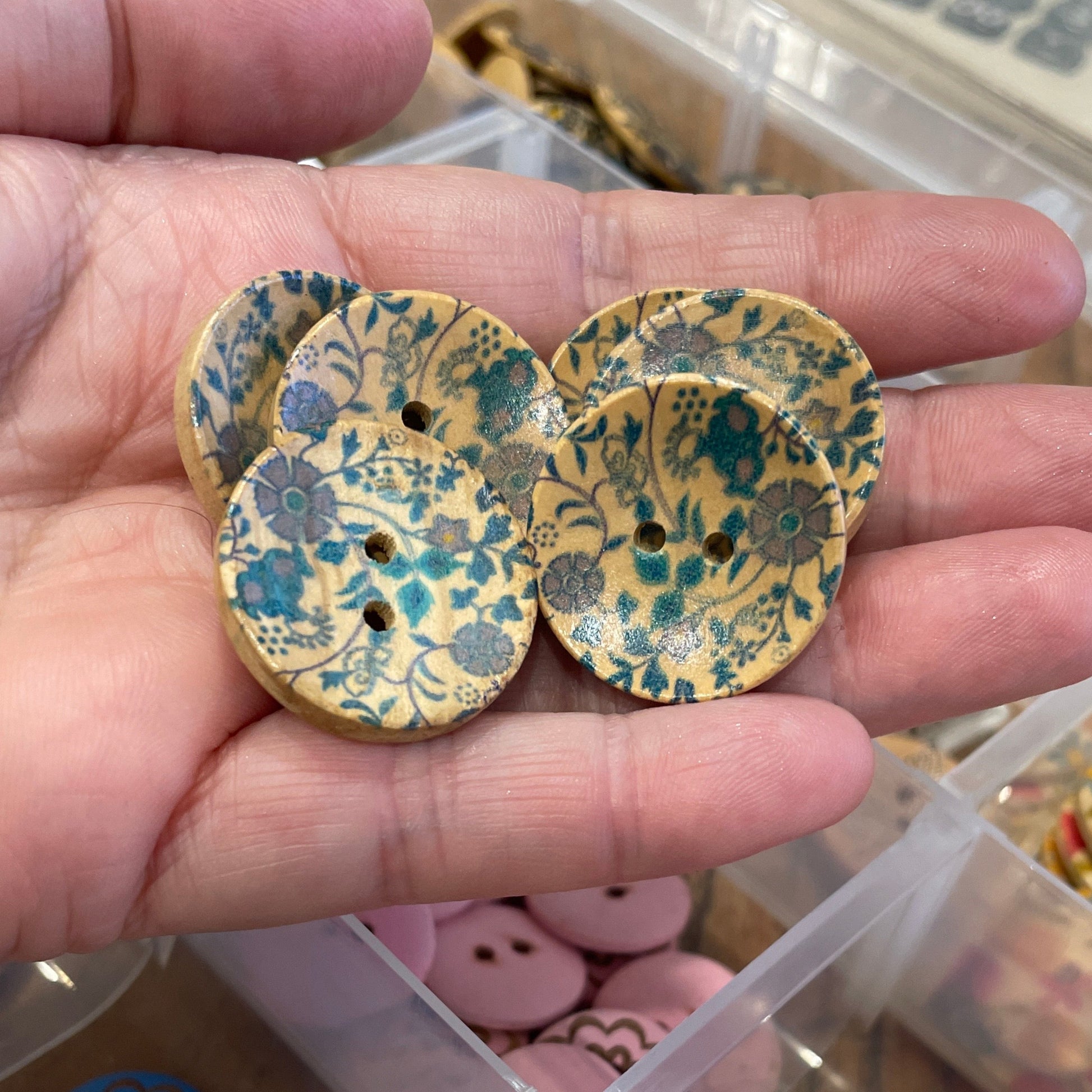 Hand holding decorative buttons with a container of assorted buttons in the background.