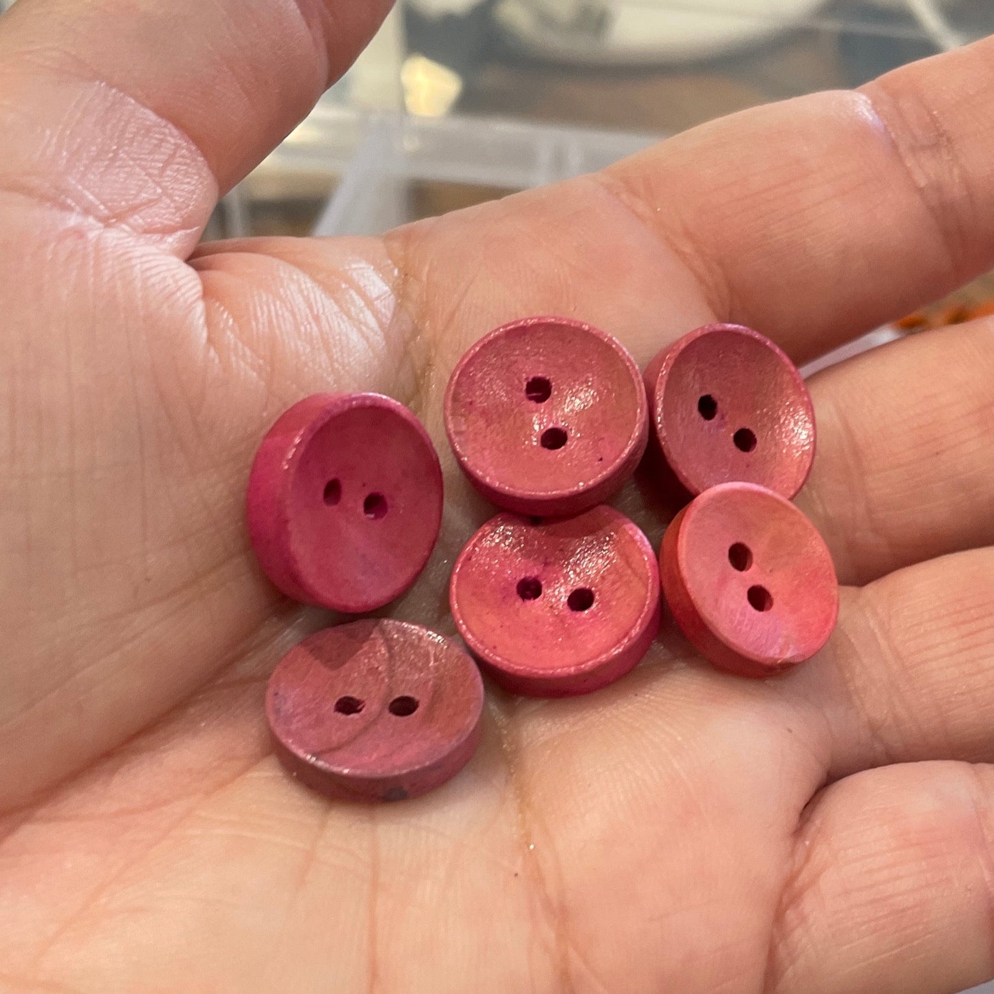 Hand holding pink buttons with a container of buttons in the background