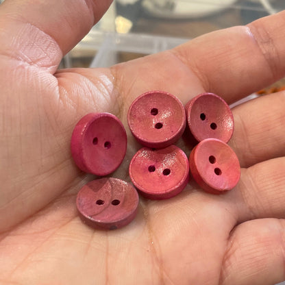 Hand holding pink buttons with a container of buttons in the background