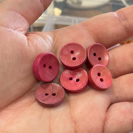 Hand holding pink buttons with a container of buttons in the background